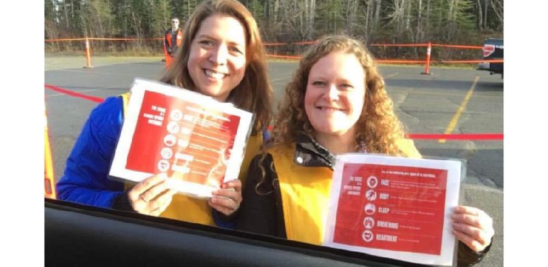 Kyla and Tiffany outside in a parking lot smiling and holding up their NARCAN certificates.