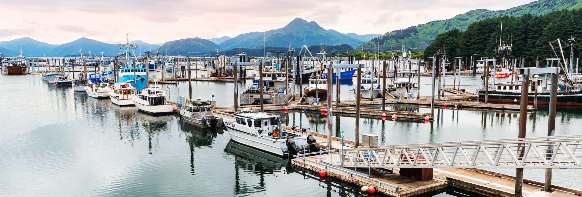 Boats in Kodiak, Alaska fishing harbor with mountains in thebackground